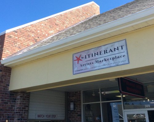 Sign for "Itinerant Artists Marketplace" on a brick building, with a warning to "Watch Your Step" visible.