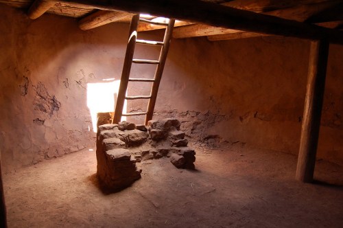 An empty, rustic room with a wooden ladder leading to a small window, illuminated by soft light.