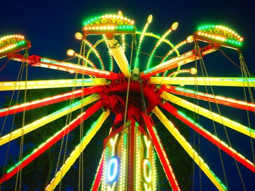 A brightly lit amusement ride with colorful lights against a night sky, featuring swinging seats.