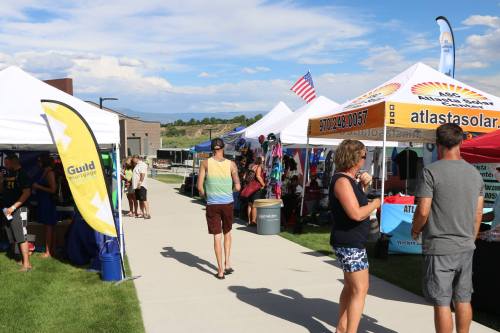 A community event with colorful tents and booths, people browsing, and a clear blue sky in the background.