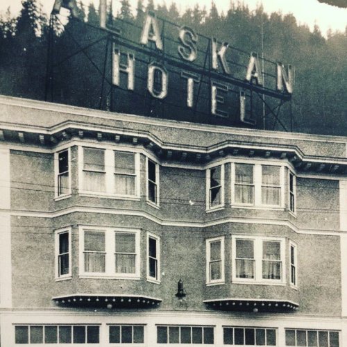 Black and white photo of the Alaskan Hotel, featuring a prominent sign and decorative windows.