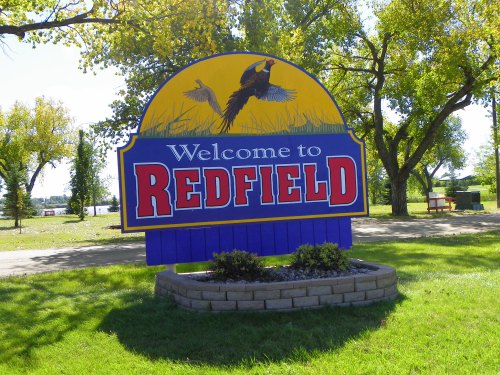 Welcome sign for Redfield, featuring a blue background, yellow top, and images of birds and trees.