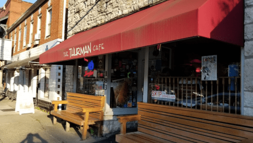 Exterior of the Thurman Cafe with a red awning and wooden benches outside, set in a brick and stone building.