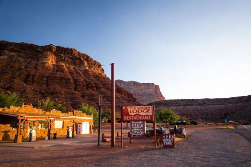 A rustic lodge and restaurant sign in a desert landscape, surrounded by red rock formations and clear blue skies.