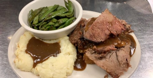 A plate with sliced roast beef in gravy, mashed potatoes with gravy, and a side of green beans.