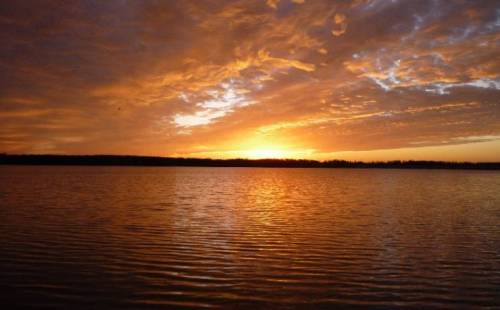 A serene sunset over a calm lake, with vibrant orange and yellow hues reflecting on the water's surface.