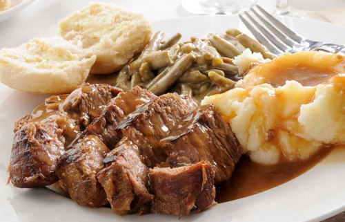 A plate of sliced roast beef with gravy, mashed potatoes, green beans, and two biscuits.