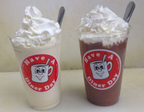 Two cups of milkshakes topped with whipped cream, one vanilla and one chocolate, both featuring a diner logo.