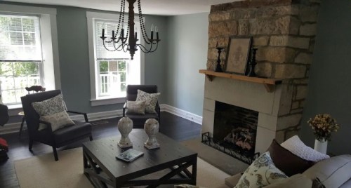 Cozy living room with stone fireplace, chandelier, and comfortable seating, featuring light blue walls and natural light.