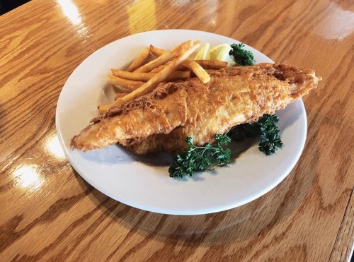 A plate of crispy fried fish with golden fries and garnished with parsley on a wooden table.