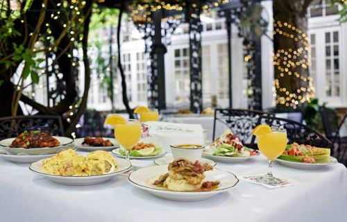 A beautifully set table with various dishes and drinks, surrounded by greenery and soft lighting.