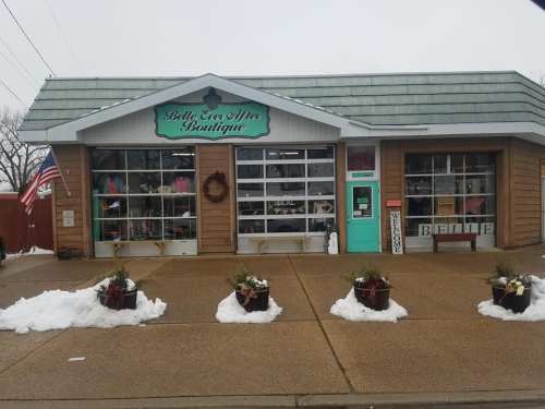 A boutique with a teal door and festive decorations, surrounded by snow and potted plants, on a cloudy day.