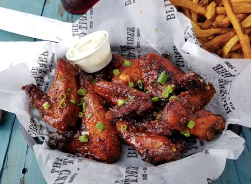 A basket of crispy chicken wings garnished with green onions and served with a side of ranch dressing.