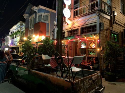 A vibrant street scene at night with colorful lights, a vintage truck, and people enjoying outdoor dining.