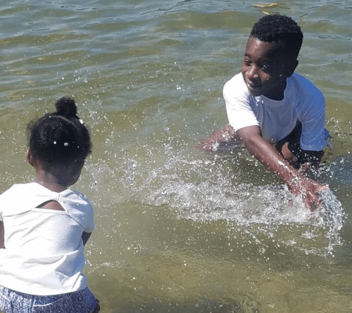 Two children play in shallow water, splashing each other and enjoying a sunny day at the beach.