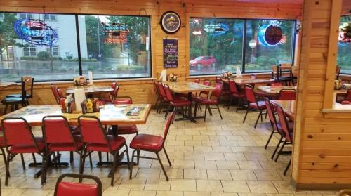 Interior of a casual restaurant with wooden walls, red chairs, and tables, featuring large windows and neon signs.