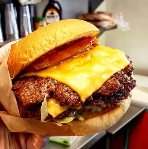 A hand holding a juicy burger with melted cheese, lettuce, and a toasted bun, set against a kitchen background.