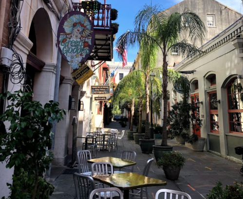 Charming alleyway with palm trees, outdoor seating, and colorful storefronts under a clear blue sky.