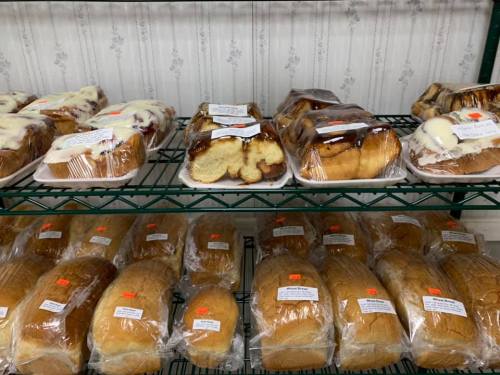 A display of various baked goods, including sweet rolls and loaves of bread, neatly packaged on shelves.