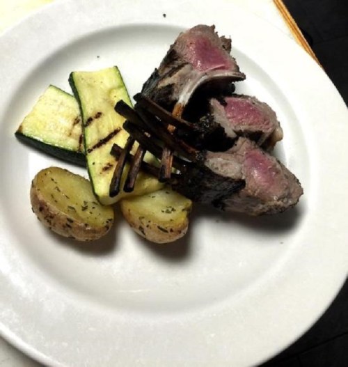 A plate with grilled lamb chops, zucchini, and roasted potatoes, garnished with herbs.