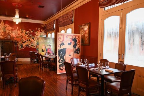 Interior of a restaurant featuring wooden tables, leather chairs, and colorful wall art in a warm, inviting atmosphere.
