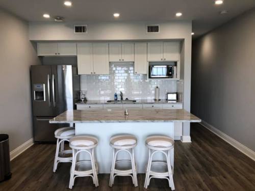 Modern kitchen with white cabinets, stainless steel appliances, a marble island, and four white bar stools.