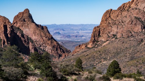 A scenic view of rugged mountains and valleys under a clear blue sky, showcasing natural rock formations and vegetation.