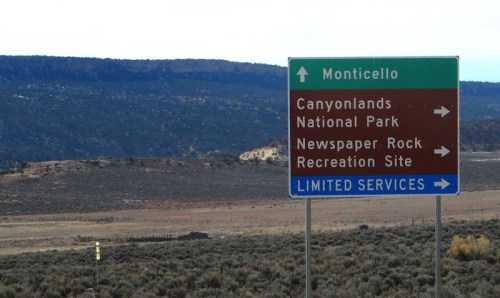 Signpost indicating directions to Monticello, Canyonlands National Park, and Newspaper Rock Recreation Site with limited services.