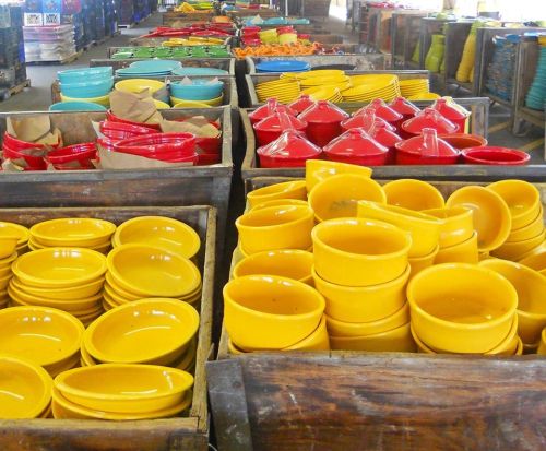 Colorful ceramic bowls and dishes in various shapes, displayed in wooden crates at a market.