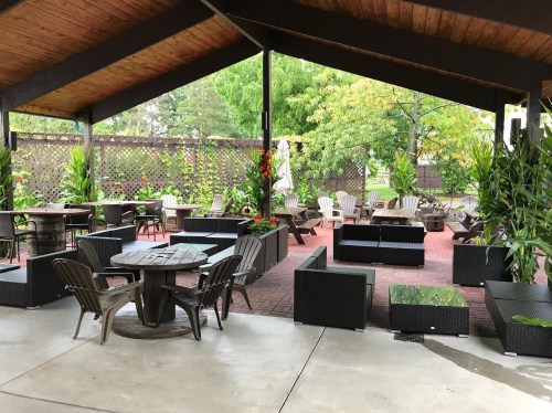 A covered outdoor patio with seating areas, surrounded by greenery and colorful plants.