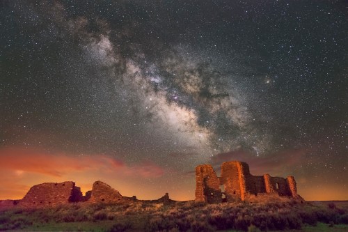 Ruins under a starry sky, with the Milky Way prominently visible above a landscape of grass and distant hills.