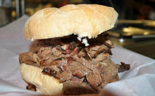 A hearty sandwich stacked with tender, sliced beef on a soft bun, served on a paper-lined plate.