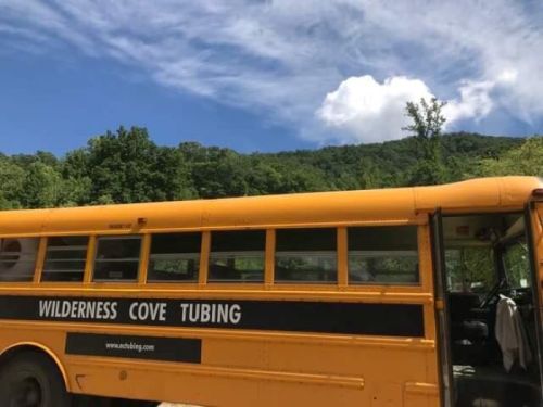 A yellow school bus parked near a lush green mountain under a blue sky with fluffy clouds.