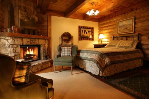Cozy log cabin bedroom with a stone fireplace, a bed, and a green armchair, featuring warm lighting and rustic decor.