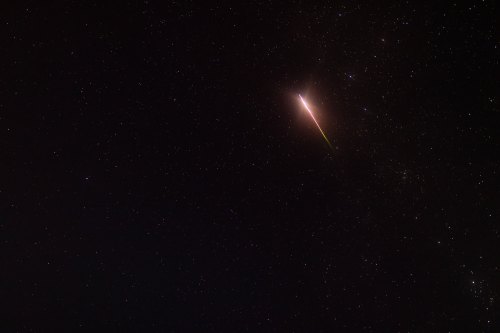A bright meteor streaks across a starry night sky, leaving a colorful trail behind it.