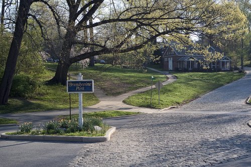 Sign for Brandywine Park with a winding path and a house in the background, surrounded by greenery and trees.