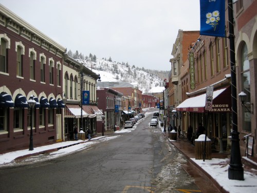 Snow-covered street lined with historic buildings and shops, with a mountain backdrop in a quaint town.