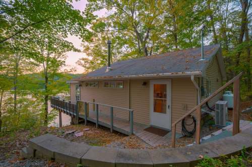 A cozy lakeside cabin surrounded by trees, featuring a wooden deck and a serene view of the water at sunset.