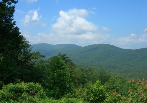 Lush green mountains under a blue sky with fluffy clouds, showcasing a serene natural landscape.