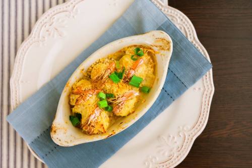 Baked shrimp dish topped with green onions, served in a white dish on a blue napkin.