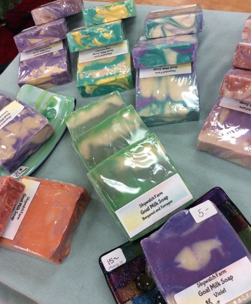 A variety of colorful handmade soaps displayed on a table, each labeled with prices and descriptions.