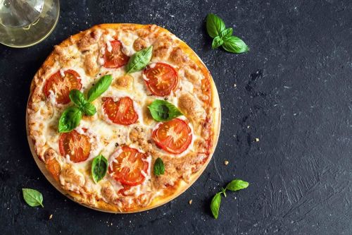 A freshly baked pizza topped with tomatoes and basil on a dark surface.