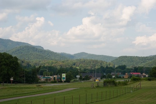 A scenic view of rolling green hills and mountains under a cloudy sky, with a small town visible in the foreground.