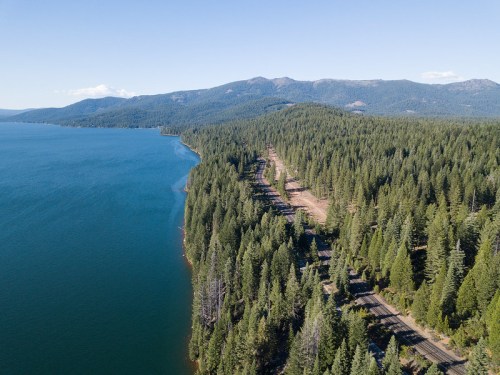 Aerial view of a serene lake bordered by dense evergreen forests and a winding road along the shoreline.