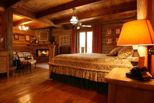 Cozy log cabin bedroom with a large bed, warm lighting, a fireplace, and rustic wooden decor.
