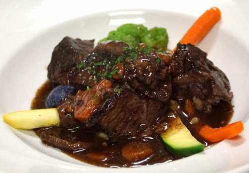 A plate of tender beef stew with vegetables, garnished with herbs and served in a rich brown sauce.