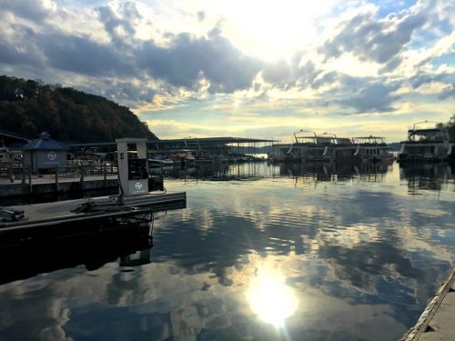 A serene marina at sunset, with boats docked and clouds reflecting on the calm water.