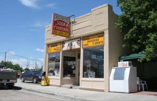 A vintage storefront with a sign reading "Chugwater Soda Fountain," featuring food, drinks, and merchandise.