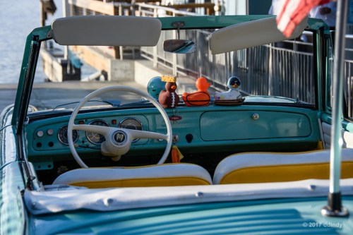 Interior of a vintage convertible car with a steering wheel and colorful plush toys on the dashboard.