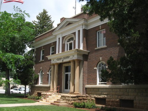 Historic brick building with columns, labeled "San Juan," surrounded by trees and a clear blue sky.